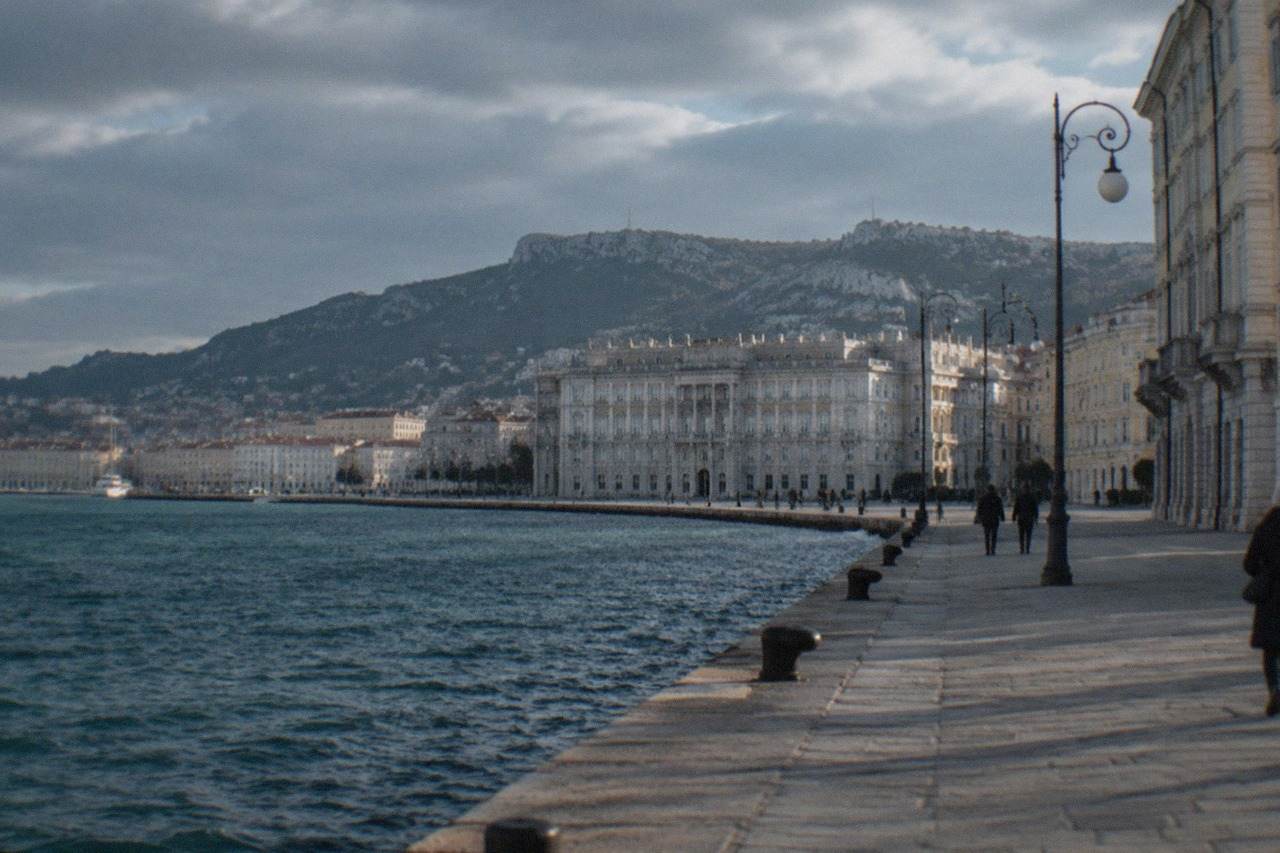 The seafront of Trieste under a heavy sky, with the Gulf of Trieste and the waterfront promenade in view