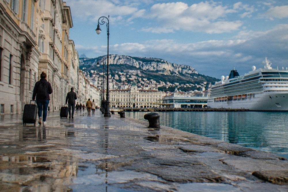 Travellers with suitcases walking along the seafront near the Trieste cruise terminal