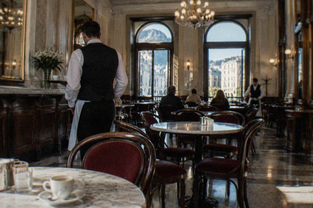 A historic Italian cafe interior in Trieste with marble tables, chandeliers and waiters serving coffee