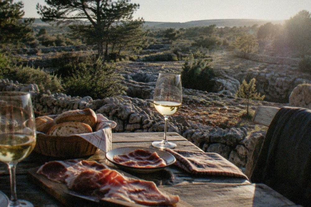 A farmhouse table on the Karst plateau set with glasses of white wine, bread and cured ham
