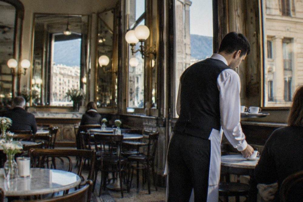 A historic coffee house interior in Trieste with marble tables, mirrors and a waiter serving espresso