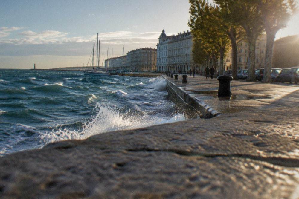 Waves breaking along the Trieste seafront promenade on a windy day, with whitecaps on the Gulf of Trieste