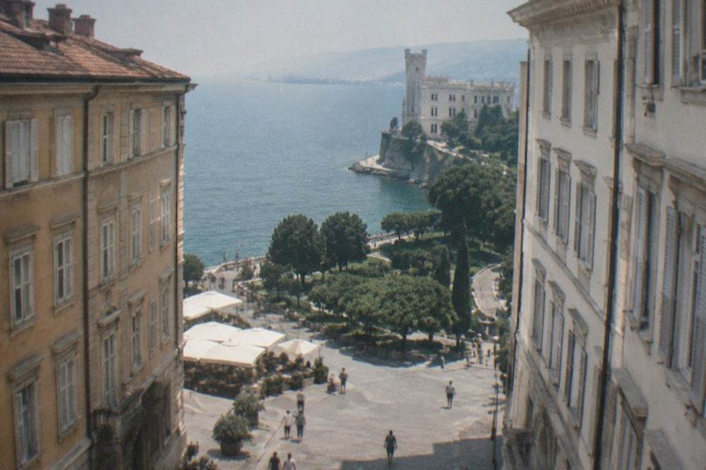 A white castle on a seafront promontory above a park of trees and paths along the Adriatic