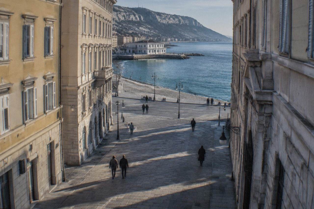 A quiet stony beach on the Trieste seafront with calm Adriatic water and a low white building