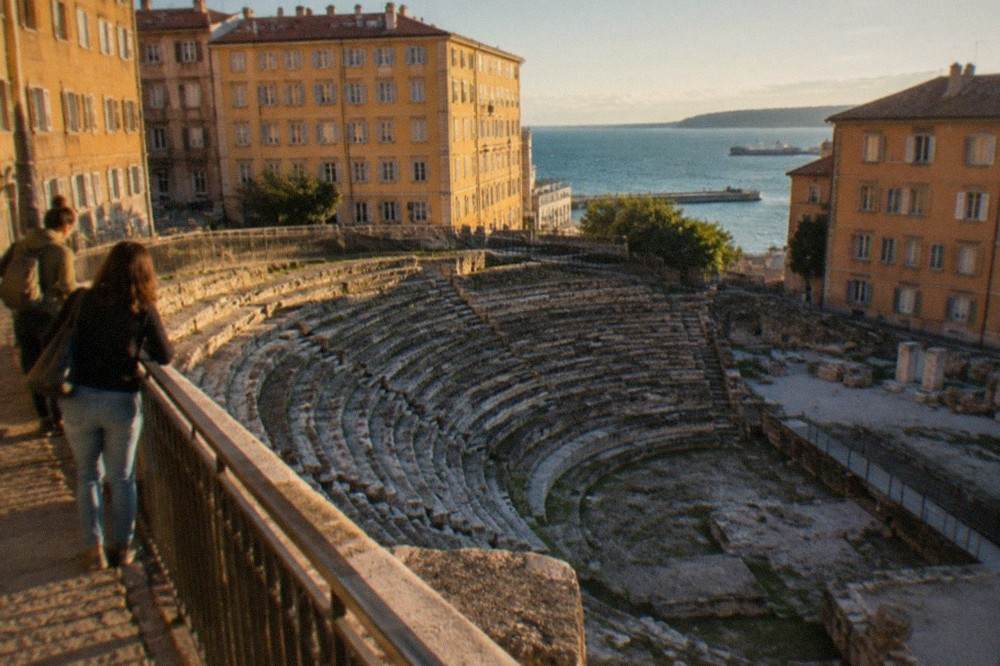Visitors looking down at the stone seats of the Roman theatre of Trieste from the street above