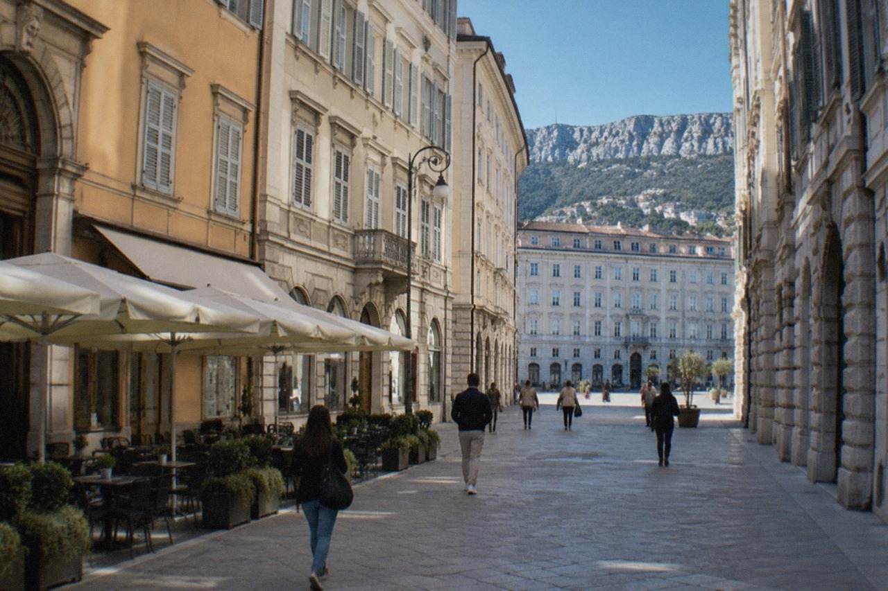 Street scene in central Trieste with historic café facades and people walking past elegant Austrian-era buildings