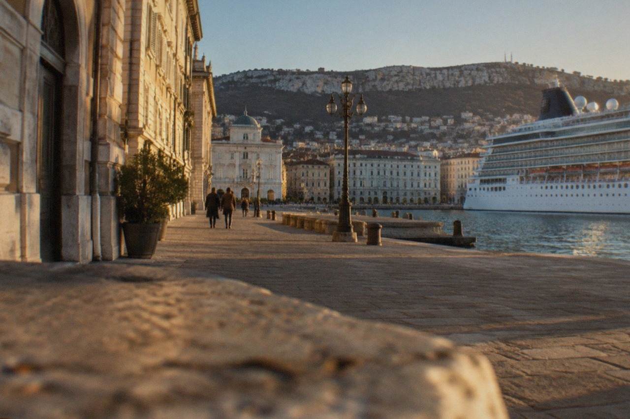 A cruise ship tied up along the Trieste waterfront with the city's neoclassical seafront buildings behind it