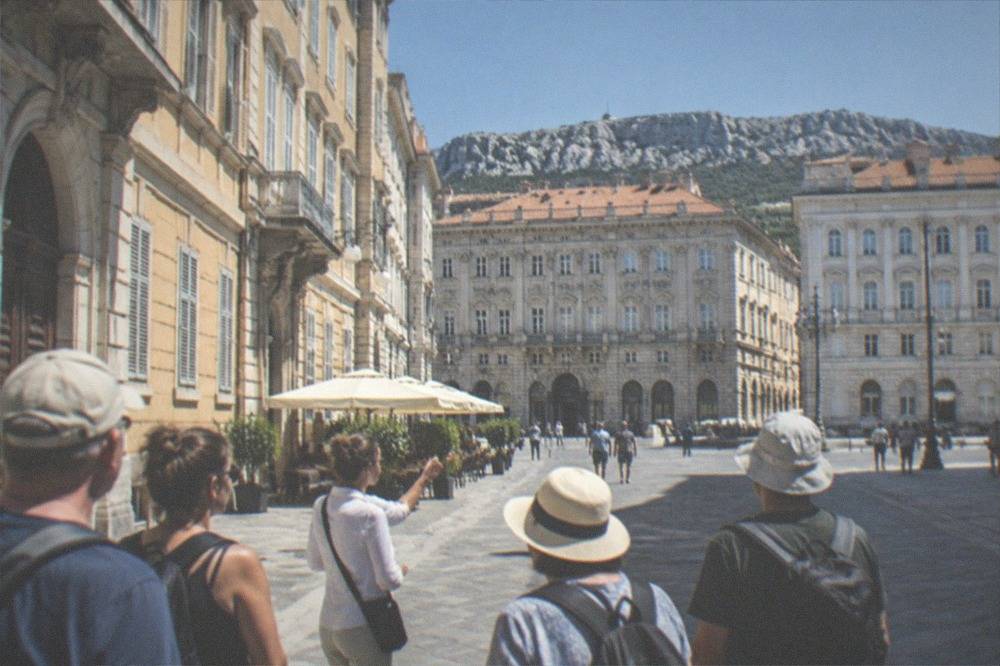 A guided walking group pausing in a Trieste square with historic facades around them