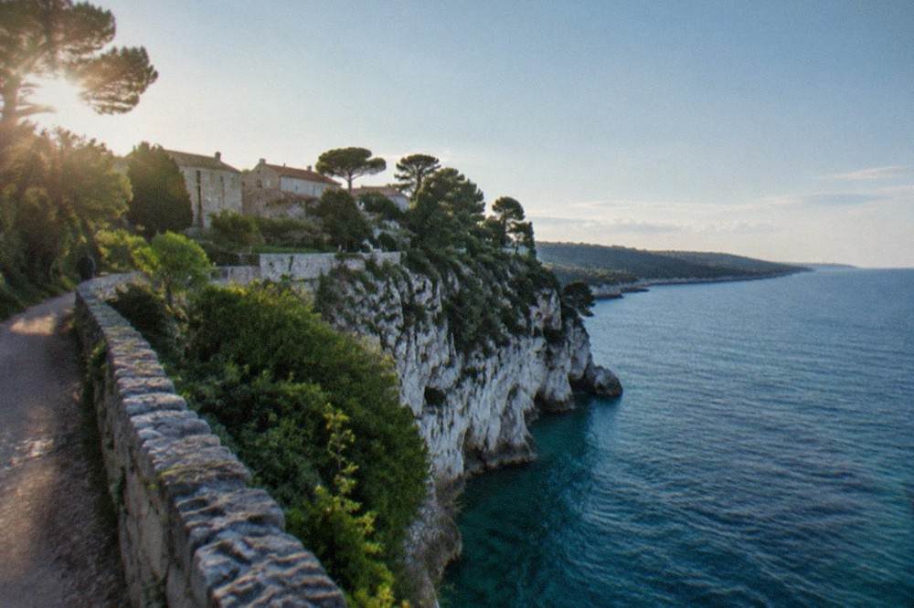 A white limestone cliff dropping into clear blue-green Adriatic water with a path along the top