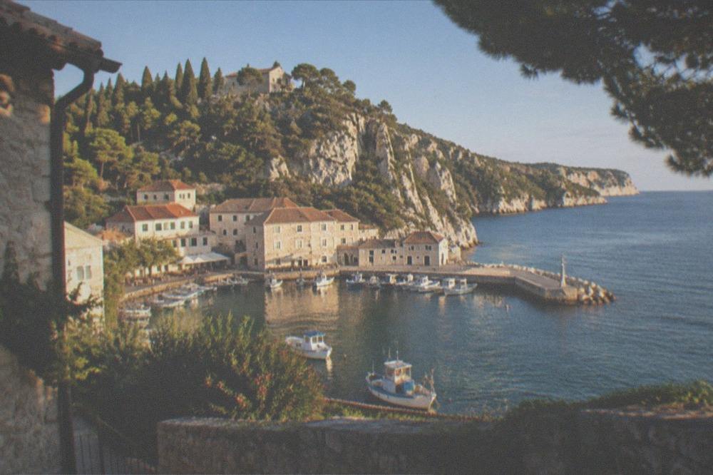 A small marina with fishing boats and stone seafront buildings at a village below cliffs