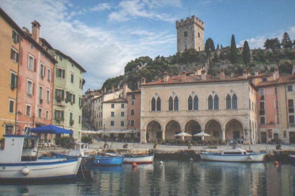 A stone tower and section of the old town walls above the rooftops of Muggia