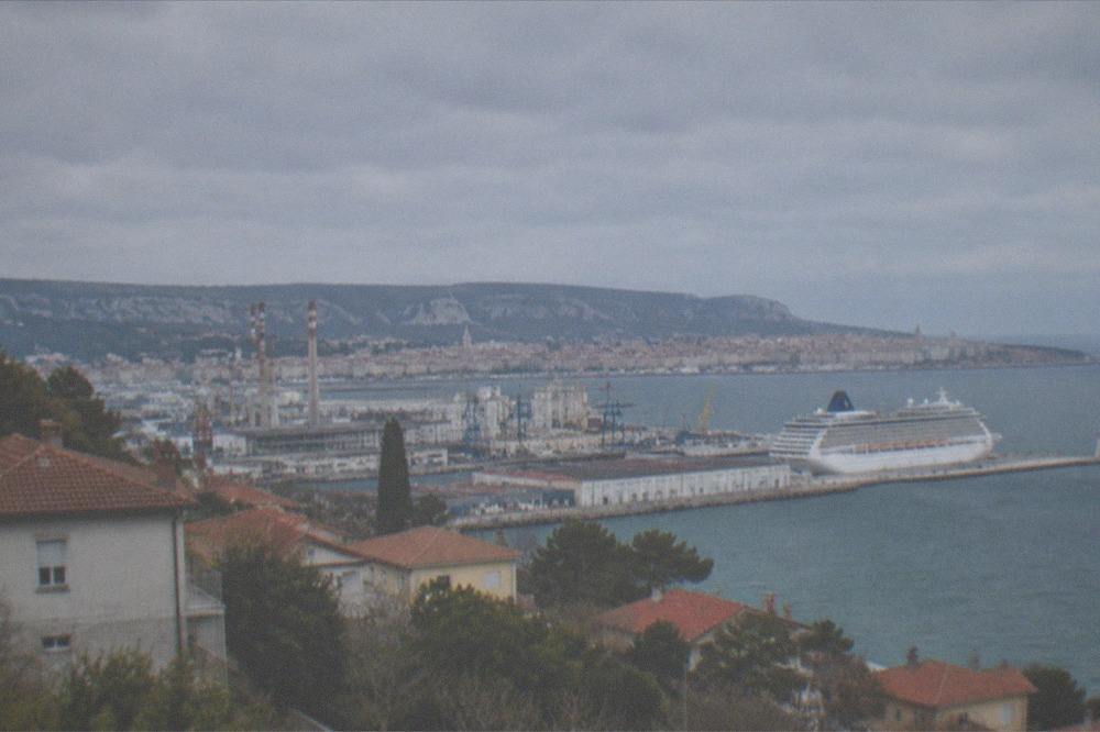 A cruise ship tied up at a long concrete pier with a historic city skyline behind it