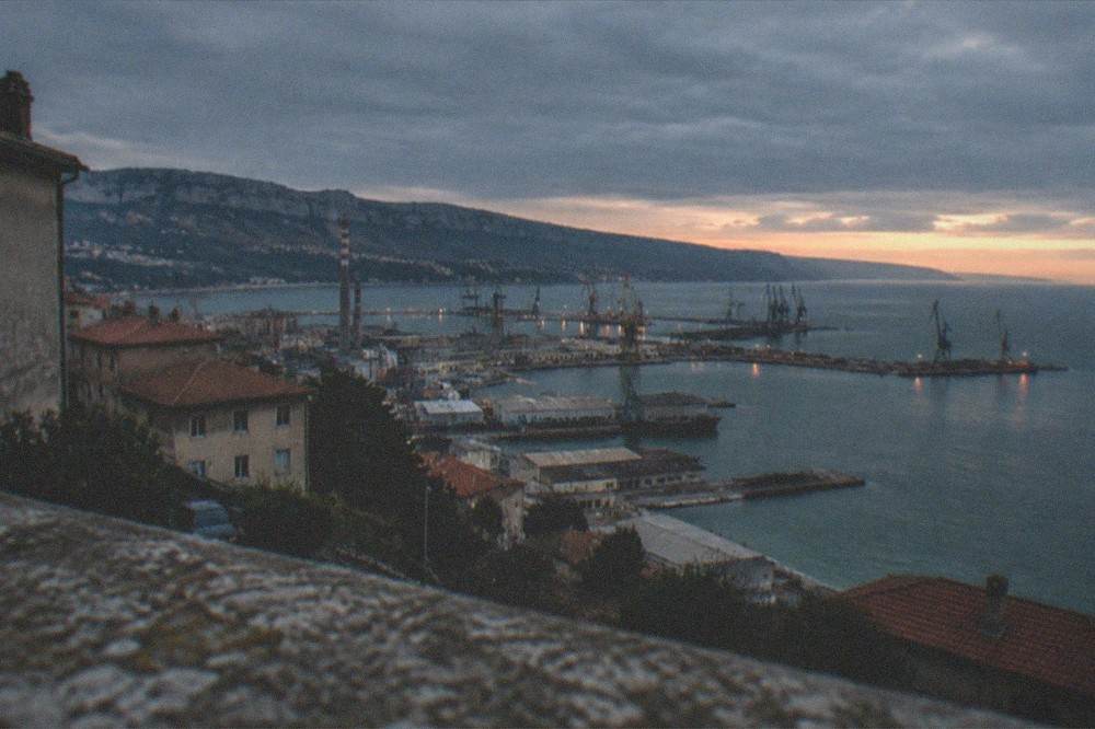 An evening view of harbour water with distant cranes silhouetted against a fading sky