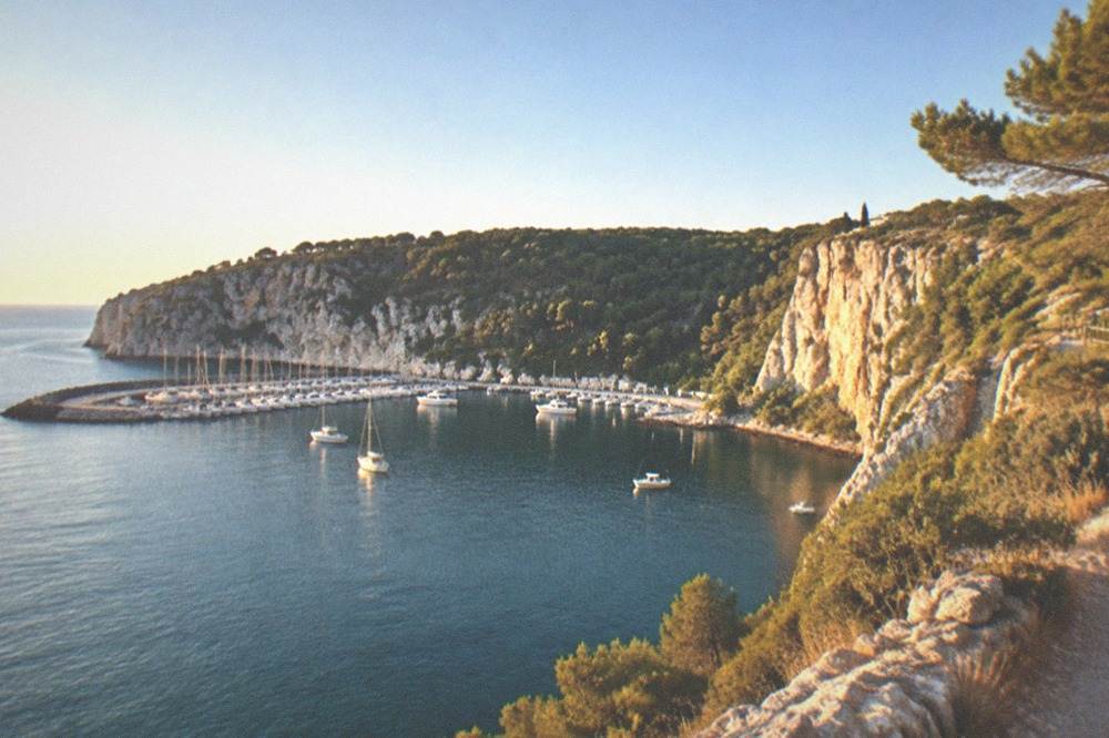 A cliff-top path above the sea with pale rock faces dropping to blue water below