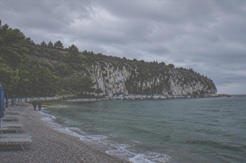 Empty beach chairs and a calm sea in early autumn light along a pine-backed shore