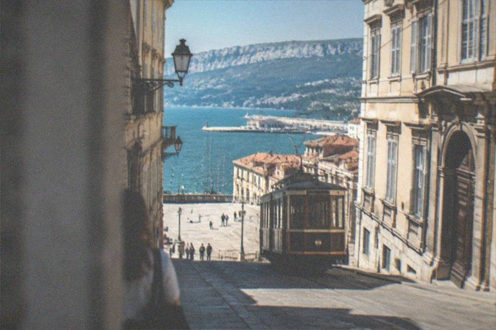 A vintage tram with wooden panelling climbing a hill above red rooftops and the sea