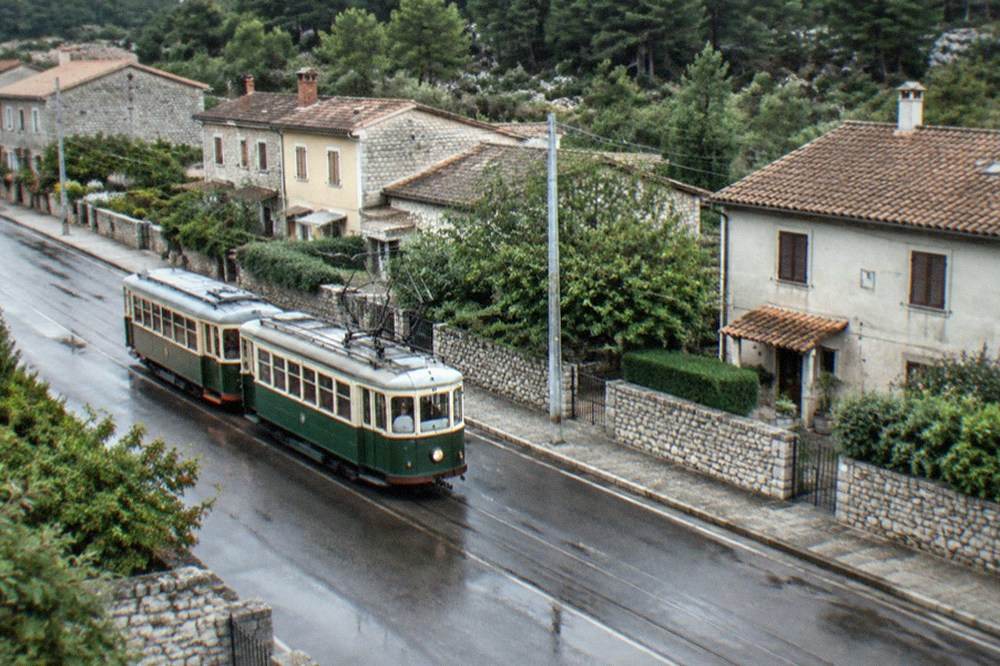A vintage two-car tram on a street at the foot of a hillside town