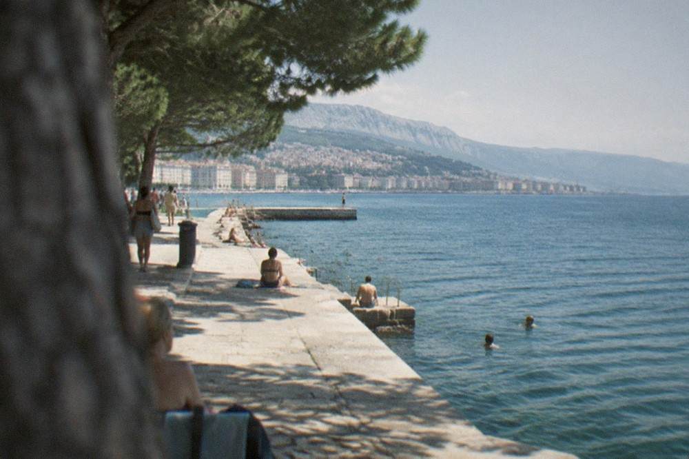 A stone seawall and calm Adriatic water at a public bathing area in Trieste with the coastline stretching away