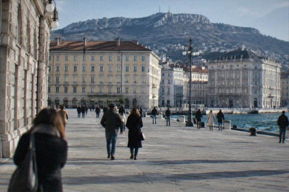People strolling along a wide seaside square in Trieste with historic buildings on three sides