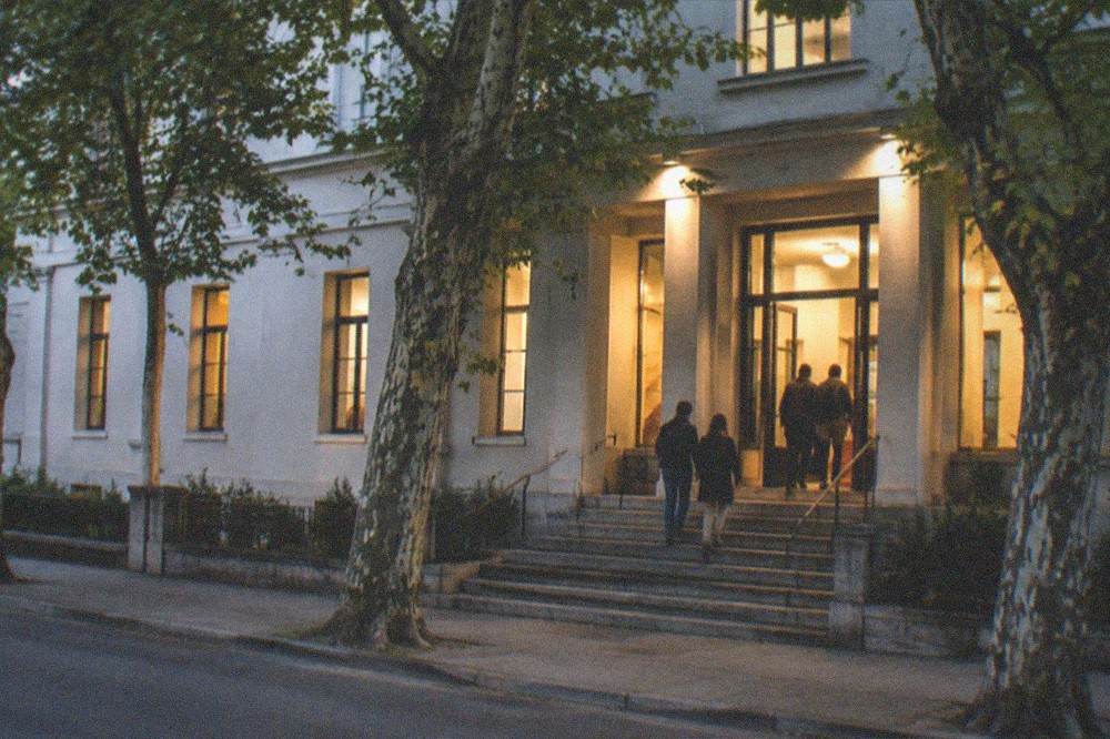 An evening view of a lit museum entrance with visitors on the steps