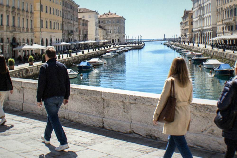 Pedestrians crossing the Ponte Rosso bridge over the Canal Grande with cafès and apartment buildings on the banks