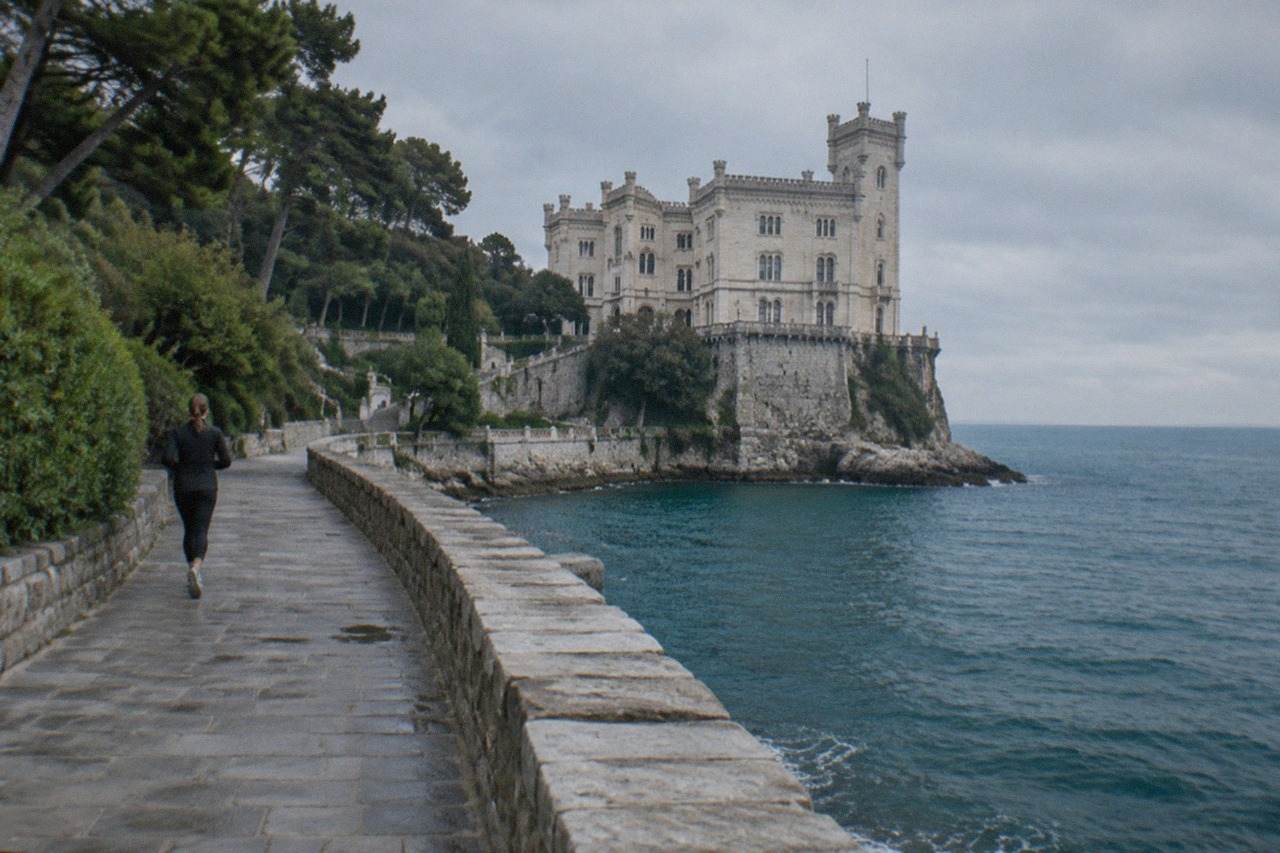A white seaside castle with towers standing above a park of trees on a headland above the sea