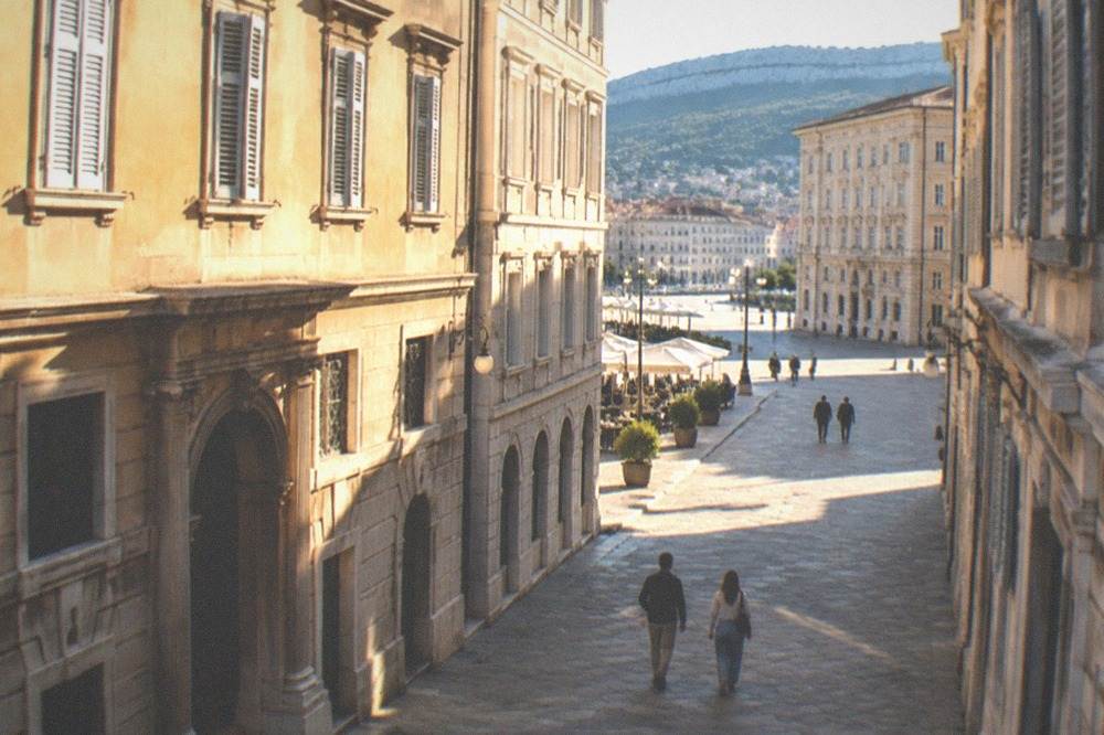 Two visitors walking between historic museum buildings in central Trieste on a sunny morning