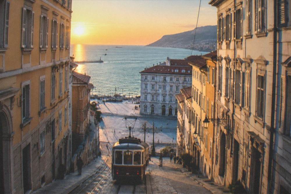 A tram descending toward the city at sunset with the sea glowing on the horizon