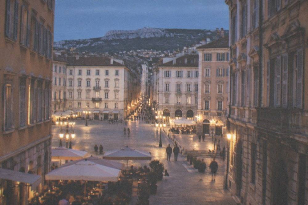 People sitting at outdoor cafe tables in a Trieste square in warm evening light