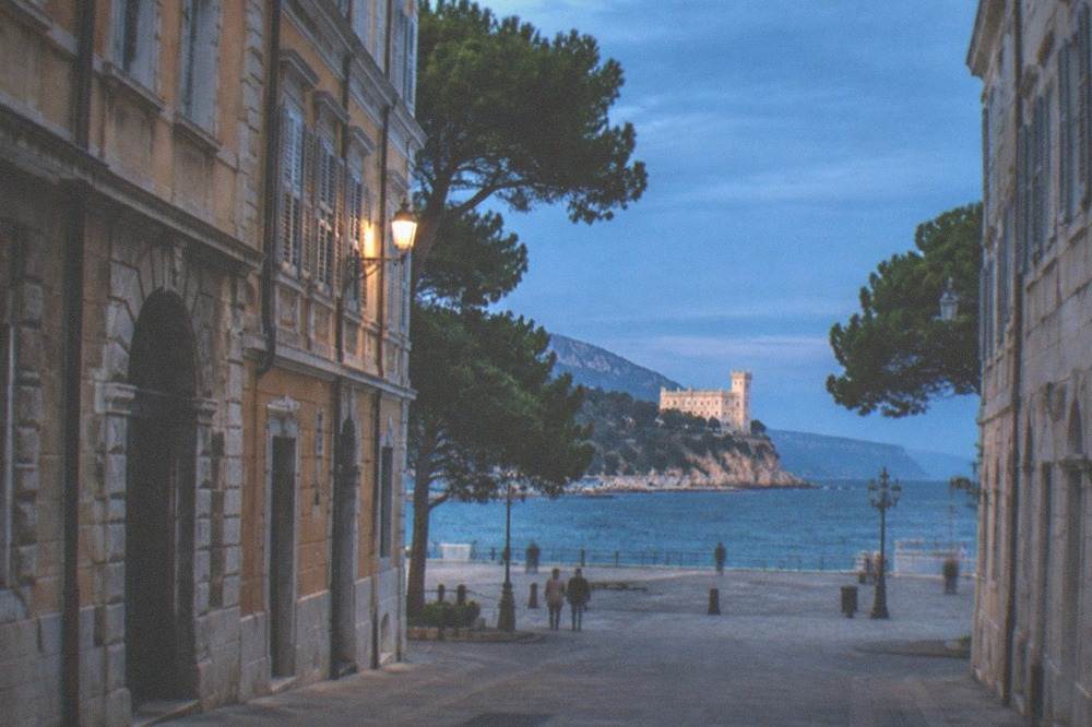 A white castle on a promontory above the Adriatic Sea seen through pine trees