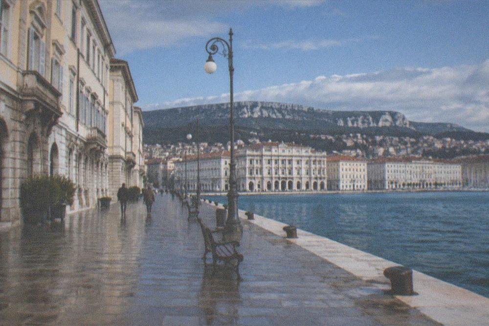 A waterfront promenade in Trieste with the sea on one side and historic buildings on the other