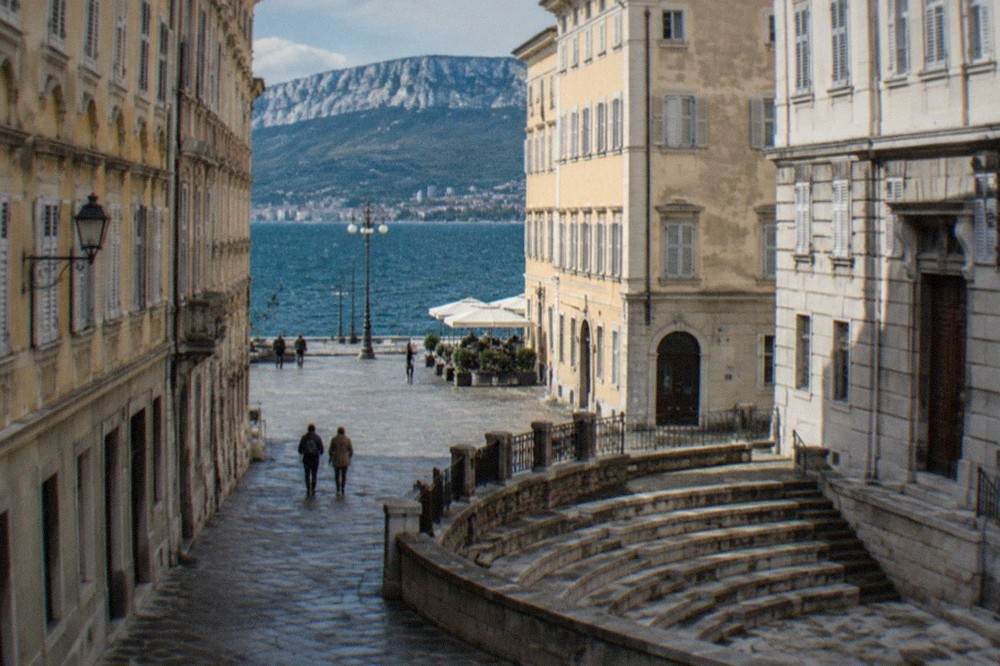 Semicircular tiers of ancient stone seating enclosed by old town houses on a narrow Trieste street