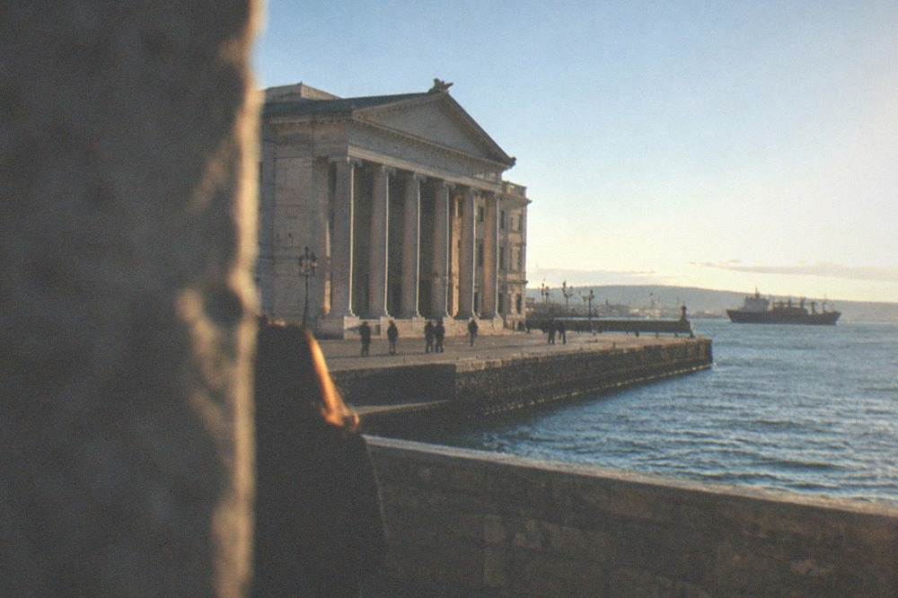 A stone castle rampart walkway above a port city with ships at anchor