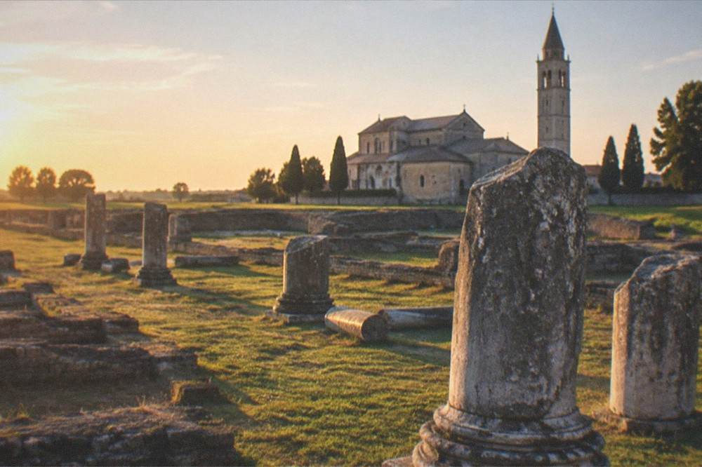 A wide flat green plain at golden hour with the silhouette of a bell tower in the distance