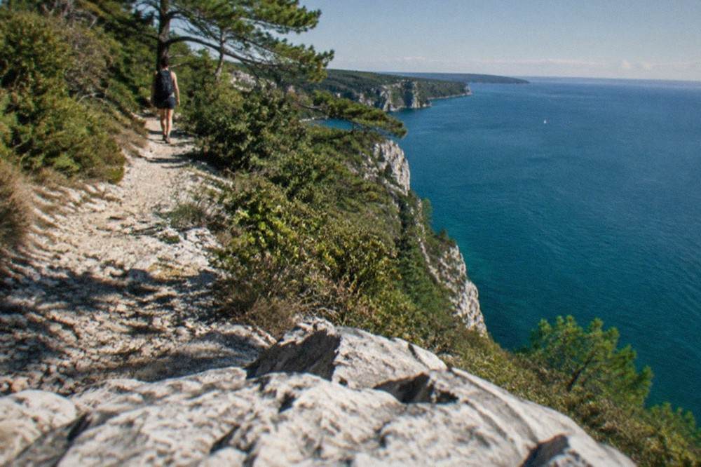 A walker on a limestone cliff path above the Adriatic with the sea below