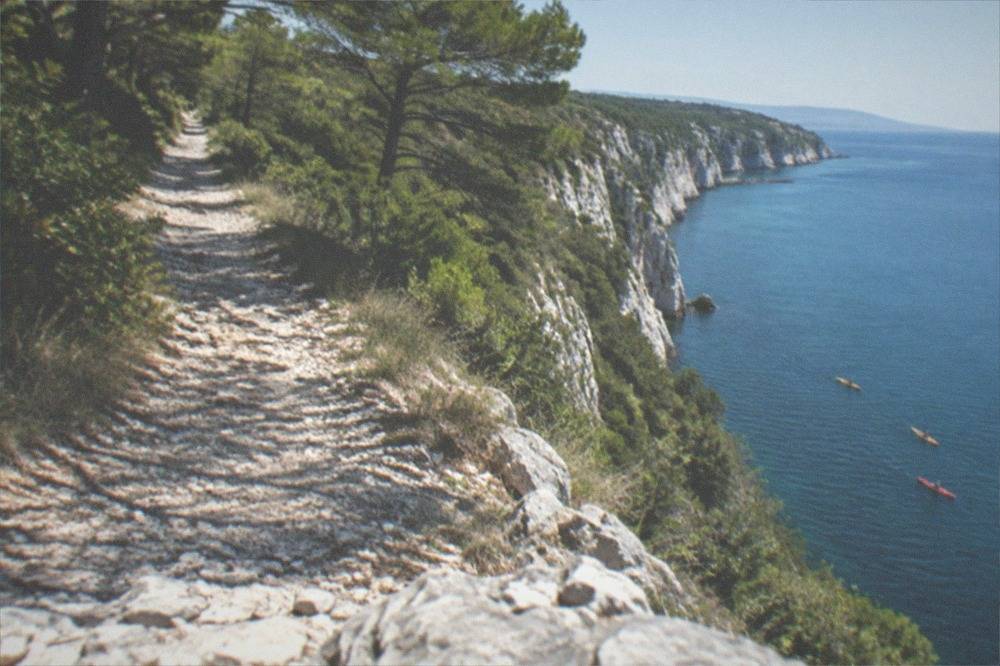 Kayaks paddling on calm blue water below white cliffs on the Adriatic coast