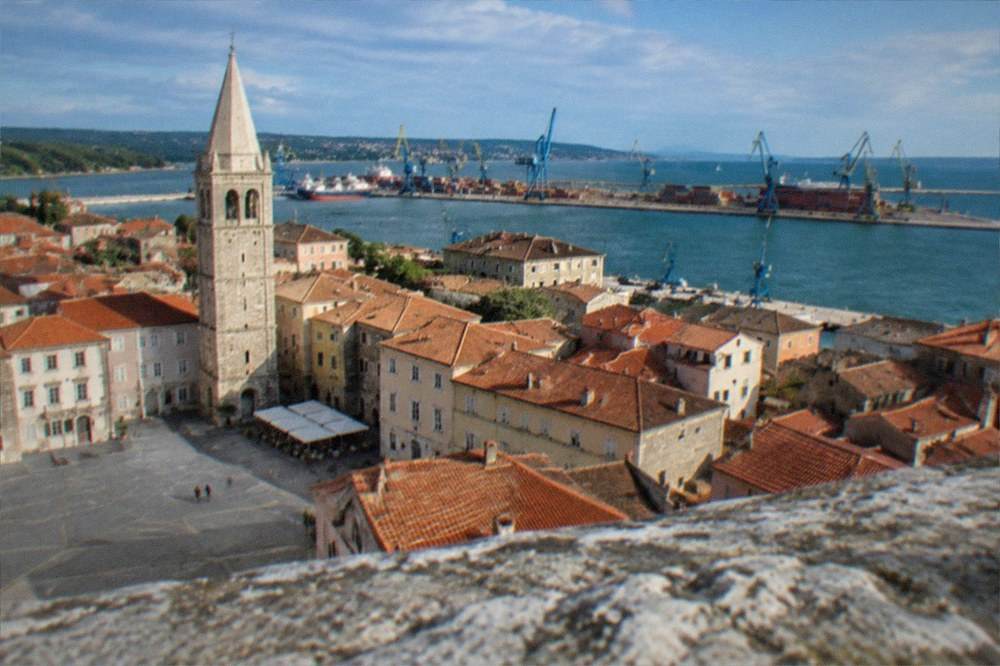 View from a bell tower over red rooftops to a harbour and sea