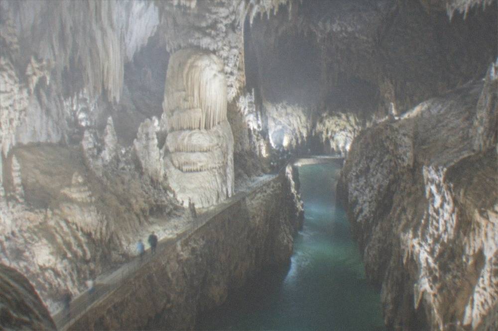 An underground canyon with a river flowing between high rock walls inside a vast cave hall