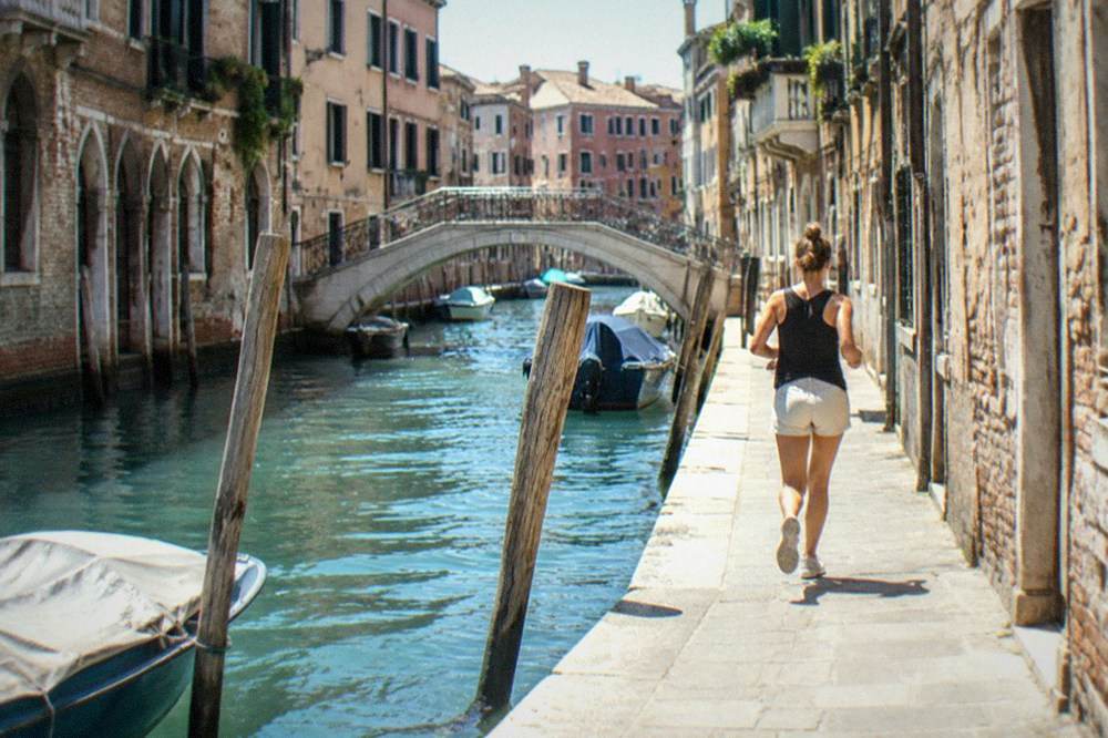 A canal in Venice with a bridge and moored boats in morning light