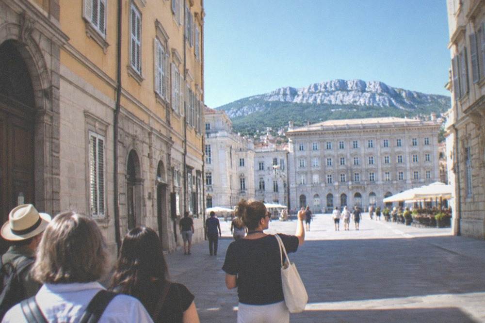 A local guide leading a small group of visitors through a Trieste square