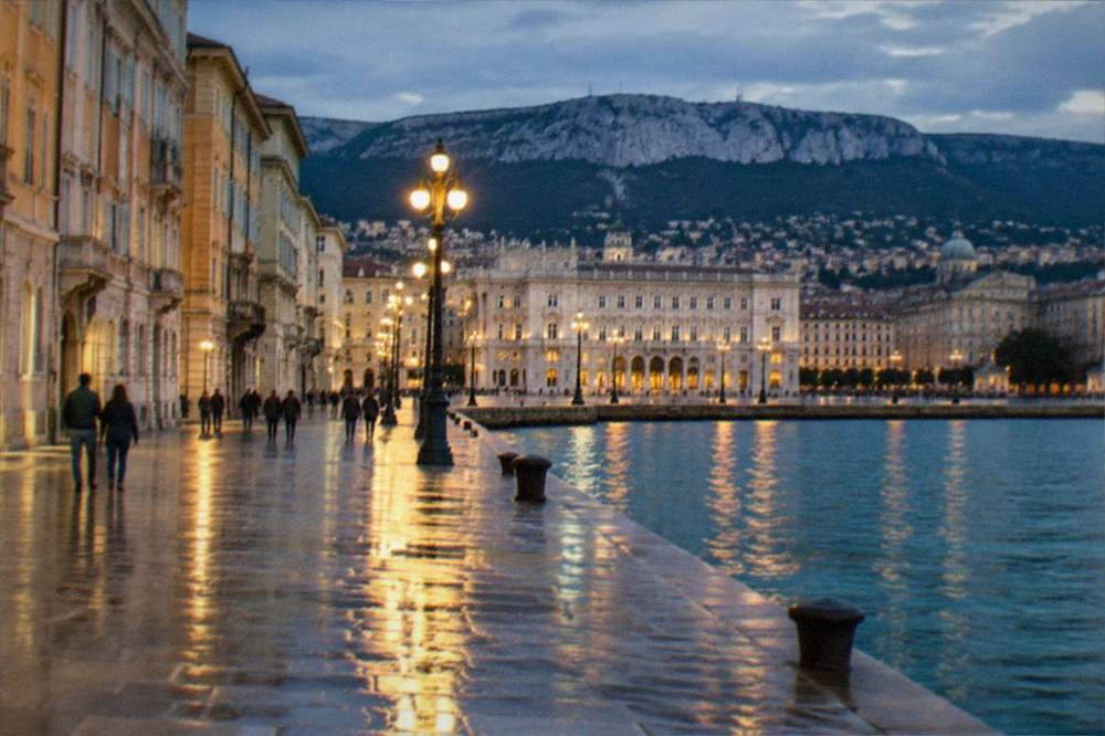 An evening view of Trieste's seafront with the lights of the wide square reflected on level paving