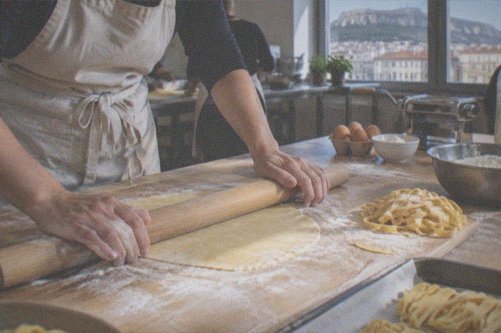 Hands rolling fresh pasta dough on a floured wooden board in a kitchen class