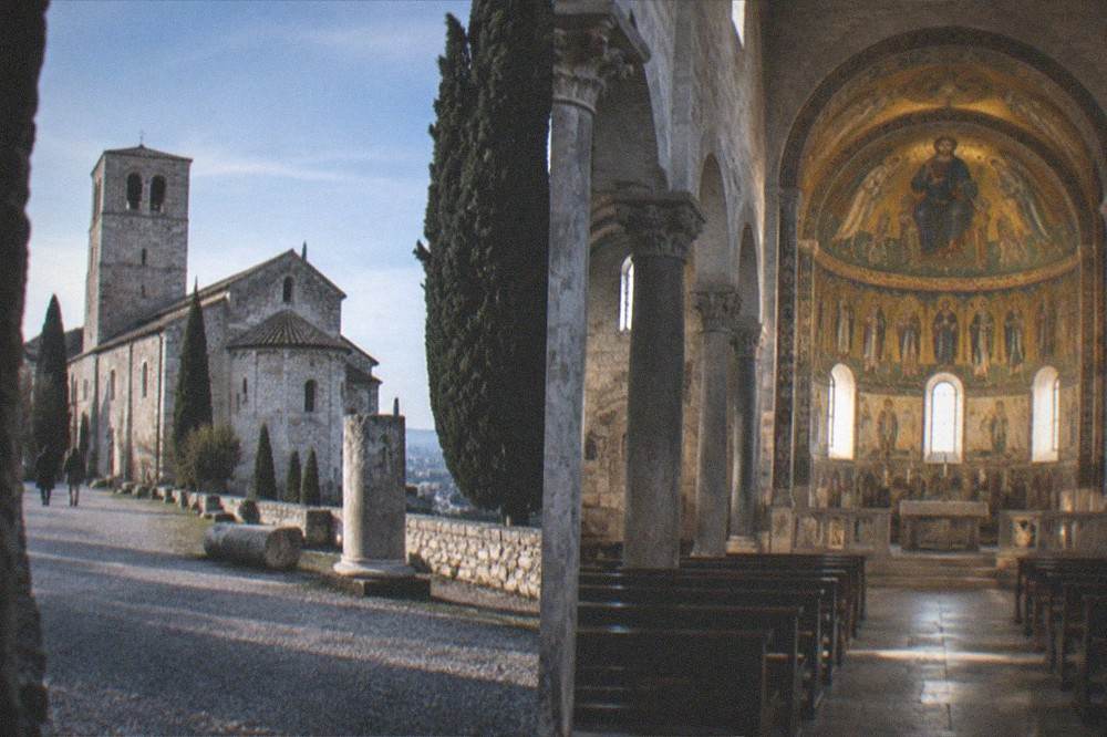 An ornate cathedral interior with mosaic decoration glowing in the apse above stone columns