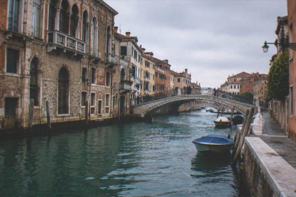 A coastal town with terracotta rooftops seen across blue water from a hillside road