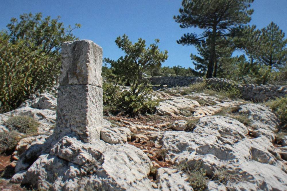 A weathered stone waymarker on the bare karst of the Carso above Trieste, pines and scrub nearby