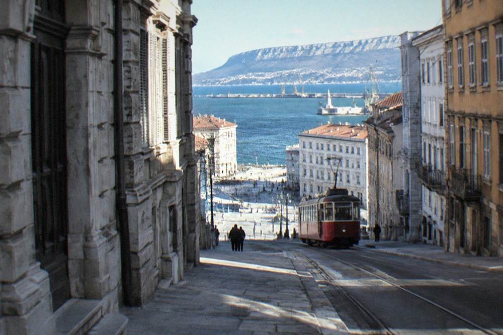 A red tram climbing a hill above rooftops with the sea in the distance
