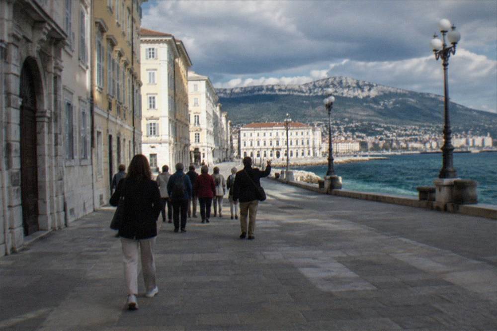 A group of visitors walking with a guide along an elegant European square beside the sea
