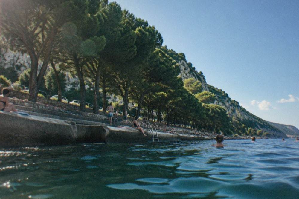 People sunbathing and swimming from concrete steps along the Barcola seafront under plane trees