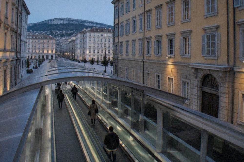 A covered walkway with moving walkways leading from an airport terminal towards a railway station