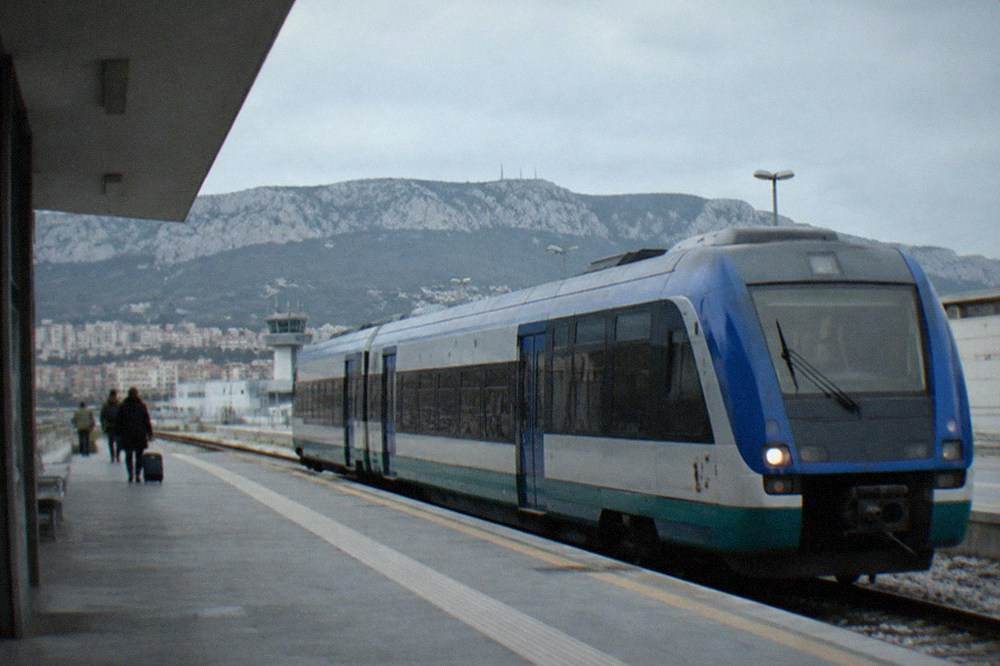 A regional train waiting at a platform outside a small airport railway station